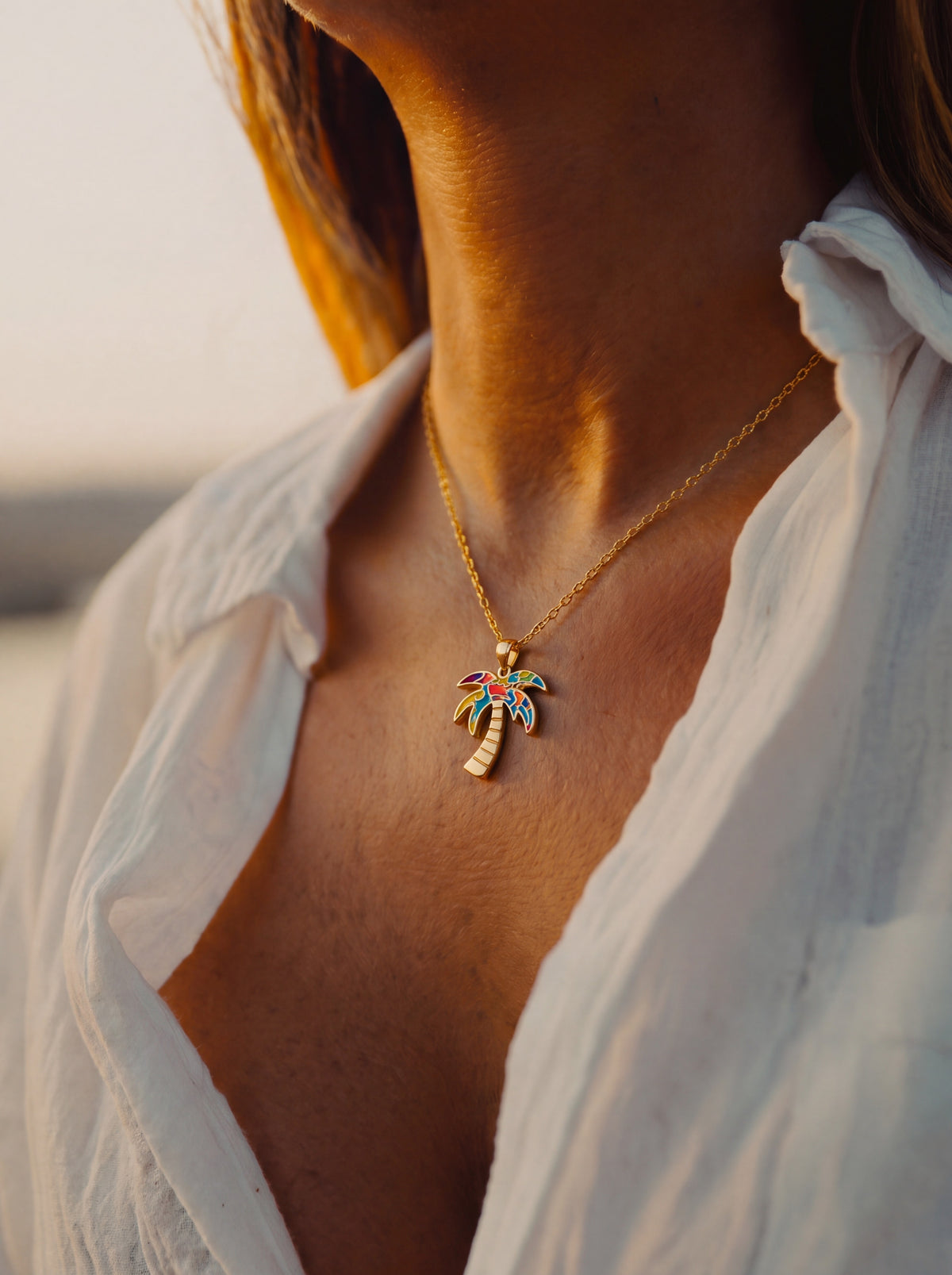 Close-up of a woman wearing the WYNWOOD BLVD Gold Graffiti Palm Tree Charm necklace inspired by Miami's Wynwood Walls at golden hour.