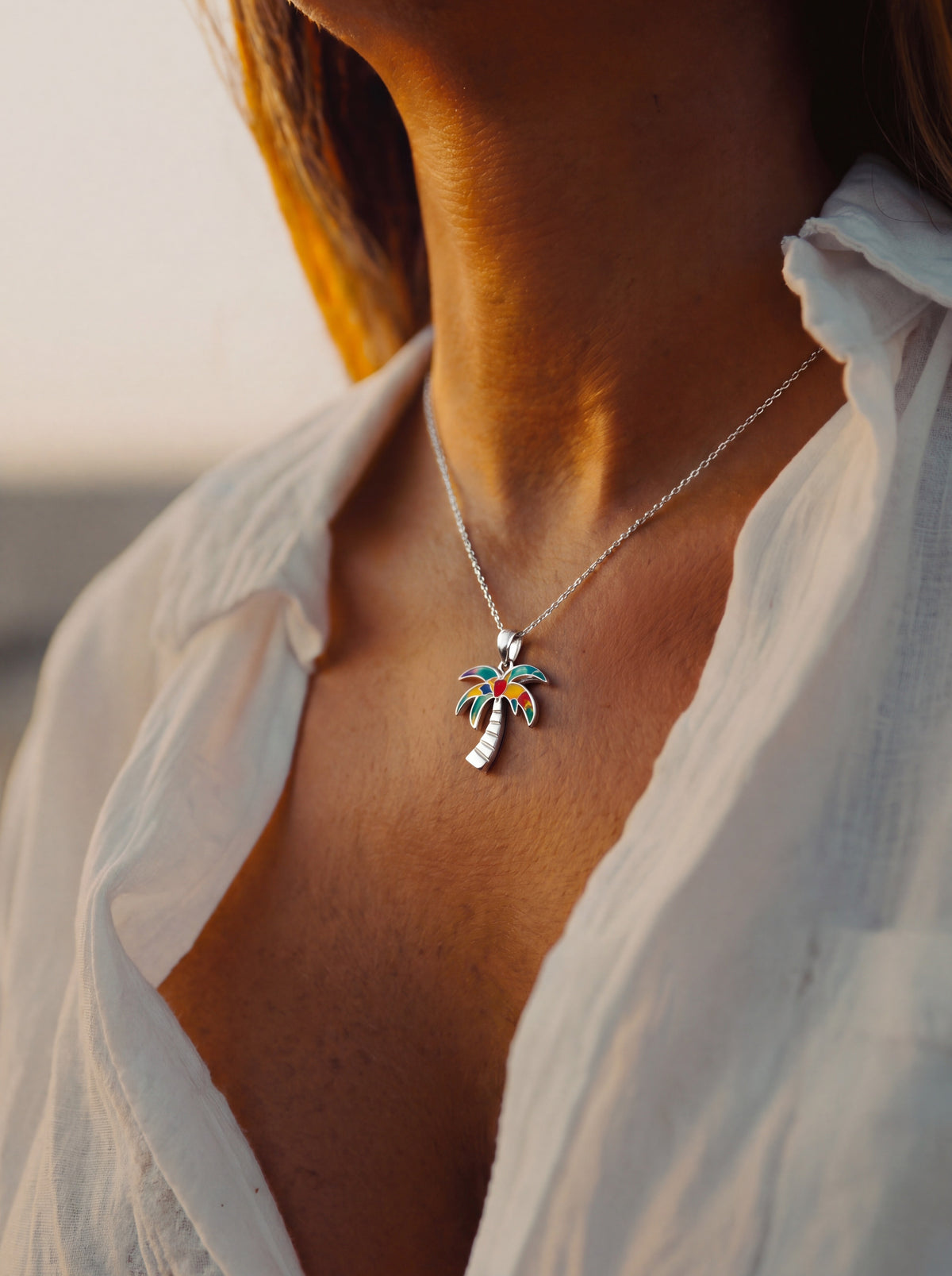Close-up of a woman wearing the WYNWOOD BLVD Silver Graffiti Palm Tree Charm necklace inspired by Miami's Wynwood Walls at golden hour.